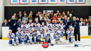 Youth hockey team in white-blue uniforms with medals and a trophy, flanked by coaches and supporters on the rink after playoffs.