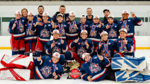 Young hockey team and coaches pose on the ice with medals and a playoff trophy, celebrating a victory.