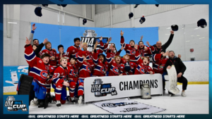 Youth hockey team celebrating a win on the ice, posing with a champions banner and raised arms in red uniforms, indoors.